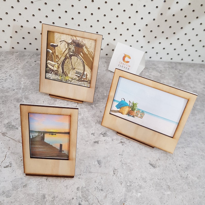 Peut inclure: Trois cadres photo en bois avec des images diff&eacute;rentes. Le premier cadre a une image d'un v&eacute;lo vintage avec un panier de fleurs. Le deuxi&egrave;me cadre a une image d'une sc&egrave;ne de plage avec un sac de plage bleu, des ananas et des tongs. Le troisi&egrave;me cadre a une image d'un coucher de soleil sur un lac avec une jet&eacute;e en bois.