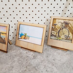Peut inclure: Trois cadres photo en bois avec des images diff&eacute;rentes. Les cadres sont tous debout sur une surface grise. L'image dans le plus grand cadre est d'un v&eacute;lo avec un panier de fleurs. L'image dans le cadre du milieu est d'une sc&egrave;ne de plage avec un ananas et une serviette bleue. L'image dans le plus petit cadre est d'un coucher de soleil sur un lac avec une jet&eacute;e.
