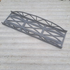May include: A grey metal bridge model with a lattice design. The bridge is made of thin metal bars and has a slightly curved shape.