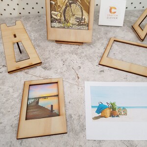 Peut inclure: Quatre cadres photo en bois avec un fond blanc et une vari&eacute;t&eacute; d'images. Les cadres sont tous de la m&ecirc;me taille et ont un design simple. Les images comprennent un v&eacute;lo, un coucher de soleil sur une jet&eacute;e, une sc&egrave;ne de plage et une carte blanche vierge avec le texte "Craftin Clever".