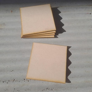 May include: A stack of four and a single square, light brown wooden coasters with a square shape and a slightly darker brown edge. The coasters are arranged on a textured, grey surface.