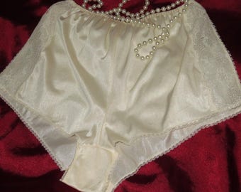 May include: White satin shorts with lace trim. The shorts have a gathered waistband and a ruffled hem.