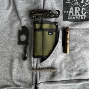May include: A gray hoodie with a black and green pocket organizer, a black multi-tool, a black bottle opener, a silver pen, and a brown flashlight. The hoodie has a patch on the front that says "USA ARC COMPANY".