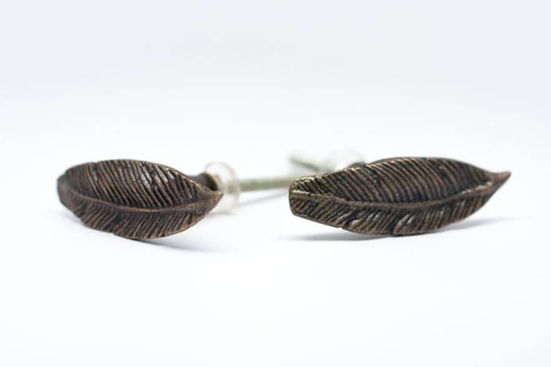 May include: A pair of bronze-coloured feather-shaped stud earrings. Each earring has detailed veining, giving a realistic appearance. The earrings are set against a white background, highlighting their intricate design and metallic finish.