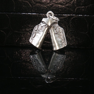 May include: A silver-toned metal charm shaped like a pair of scuba diving fins. The charm features a textured surface with detailed lines and a small circular jump ring attached at the top for hanging. The metal has a polished, reflective finish.