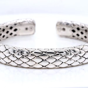 May include: A silver cuff bracelet featuring a repeating, raised scale-like pattern across the entire outer surface. The bracelet has an open-ended design with smooth, flat interior ends that show small circular indentations on each side.