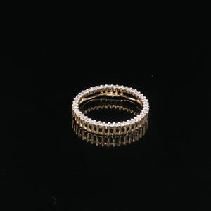 May include: A gold eternity band ring featuring a continuous row of small, clear, round-cut stones set along the entire circumference of the metal band. The ring is positioned to show its circular shape and the reflective quality of the metal.