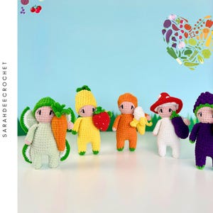 Puede incluir: Un conjunto de seis muñecas amigurumi de crochet vestidas como diferentes frutas y verduras. Las muñecas son verdes, amarillas, naranjas, blancas, moradas y rojas. Sostienen una zanahoria, una piña, un plátano, una berenjena, un rábano y una fresa.
