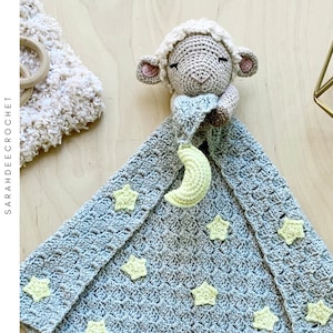 May include: A crocheted baby blanket with a gray and white color scheme. The blanket features a crocheted lamb with a crescent moon and stars. The blanket is perfect for a baby shower gift.