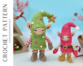 May include: Two crocheted Christmas elf ornaments, one green and one pink, with white and red striped accents. Both elves have brown boots and are standing on a light blue background.