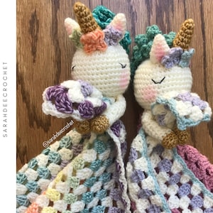May include: Two crocheted unicorn amigurumi toys with floral accents, holding a multi-colored granny square crochet baby blanket. The blanket is made with a variety of pastel colors, including pink, blue, green, and purple.