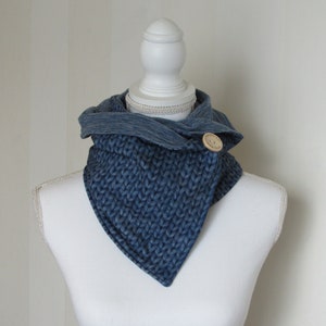 May include: A blue knitted cowl neck scarf with a wooden button closure. The scarf is displayed on a white mannequin.