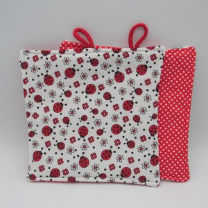 Peut inclure: Deux maniques rouges et blanches avec un motif de coccinelles. Une manique a un fond blanc avec des coccinelles rouges et des fleurs blanches. L'autre manique a un fond rouge avec des pois blancs.