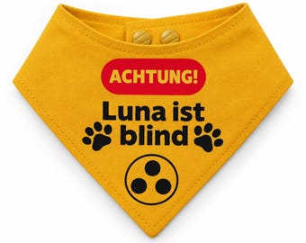 Könnte beinhalten: Ein senfgelbes, dreieckiges Halstuch für Haustiere mit zwei Druckknöpfen am oberen Rand. Der Text ACHTUNG! steht in Gelb auf einem roten Oval, gefolgt von dem schwarzen Text Luna ist blind, zwei schwarzen Pfotenabdrücken und einem Drei-Punkte-Symbol.