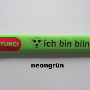 Könnte beinhalten: Ein neongrünes rechteckiges Objekt mit dem Text "ACHTUNG!" in einem roten Oval und "ich bin blind" mit Braille-Symbolen. Das Wort "neongrün" steht unten.