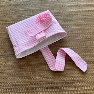 May include: A pink and white gingham fabric pouch with a matching flower accent and long tie. The pouch is open, revealing a white interior. The fabric has a classic checkered pattern.