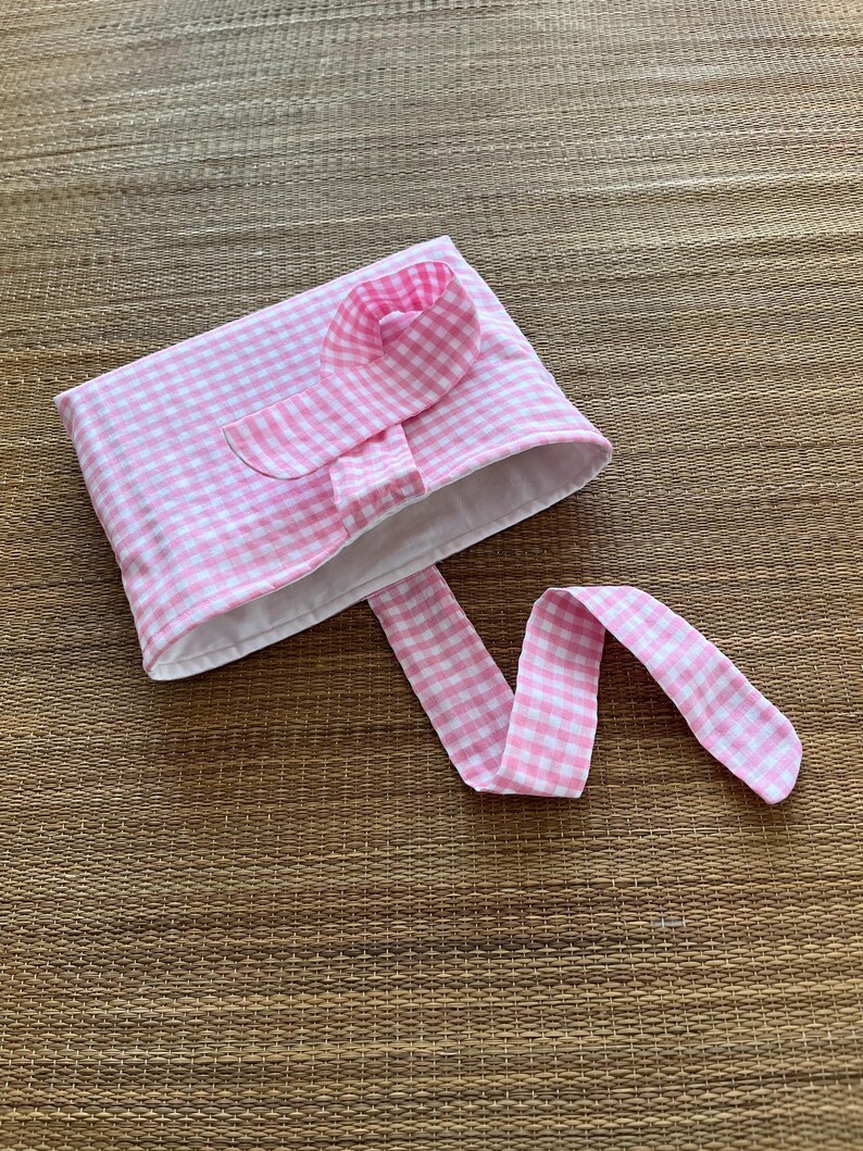 May include: A pink and white gingham fabric pouch with a matching flower accent and long tie. The pouch is open, revealing a white interior. The fabric has a classic checkered pattern.