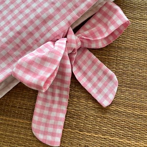 May include: Close-up of a pink and white gingham fabric with a tied bow. The bow is made of the same checkered fabric. The fabric is likely used for home decor or crafting projects.
