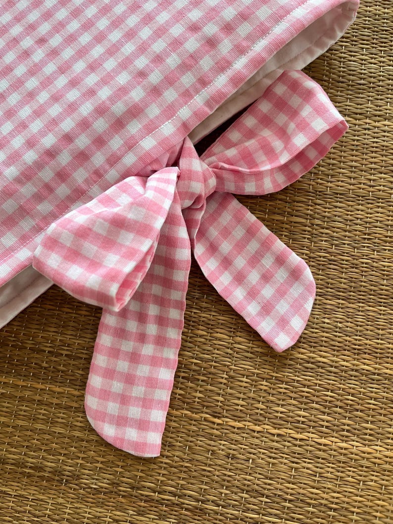 May include: Close-up of a pink and white gingham fabric with a tied bow. The bow is made of the same checkered fabric. The fabric is likely used for home decor or crafting projects.