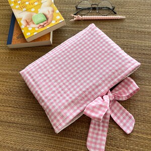 May include: A pink and white gingham pattern book sleeve with a matching bow. The image also shows a pair of round glasses, a pink stylus, and two books, one with the title "Kendime Ait G&ouml;r&uuml;nme Bir Işaret".