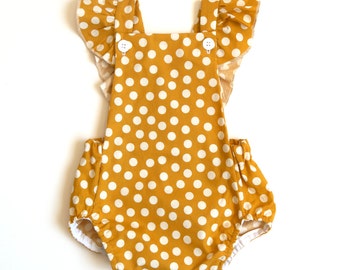 May include: A mustard yellow baby onesie with white polka dots and ruffled sleeves.