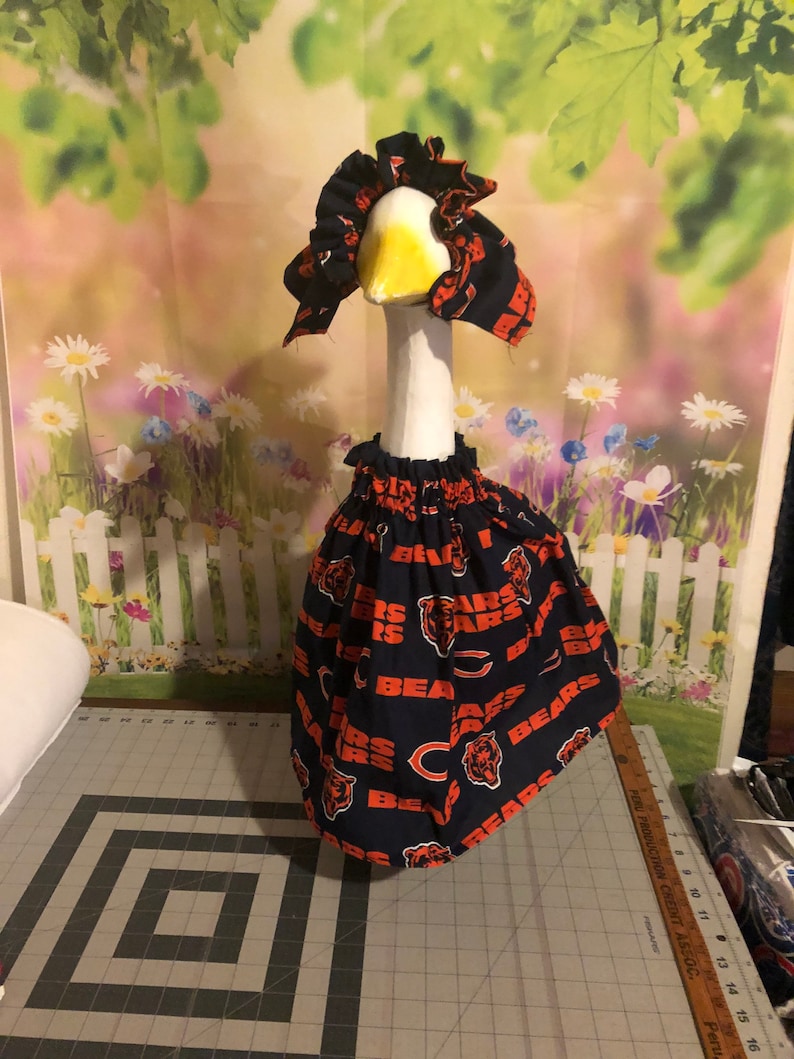 May include: A white goose wearing a blue and orange Chicago Bears themed dress and matching hat.