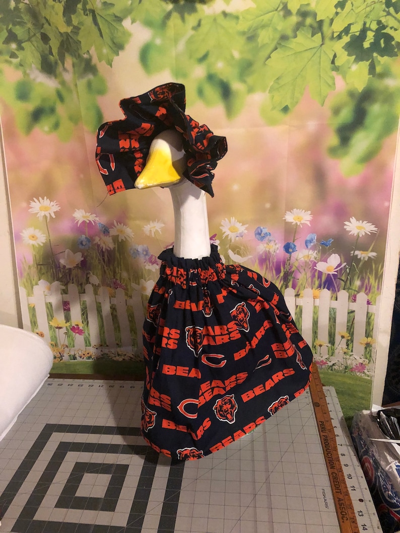 May include: A white goose wearing a blue and orange Chicago Bears themed hat and skirt.