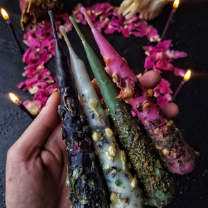 Può includere: Quattro candele coniche con cere di diversi colori e erbe e fiori incorporati. Le candele sono nere, bianche, verdi e rosa.