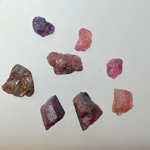 Peut inclure: Une collection de huit pierres précieuses brutes, non taillées, roses et violettes. Les pierres précieuses sont de tailles et de formes variées, certaines ayant une apparence plus arrondie et d'autres étant plus angulaires.