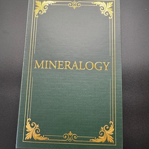 May include: A hardcover book titled "Mineralogy" with a dark green cover. The cover features gold decorative borders and corner designs. The title is in gold lettering.