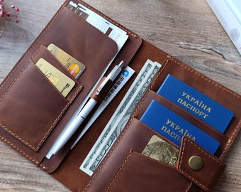 May include: A brown leather passport holder with multiple pockets for cards, cash, and a pen. The holder is open and shows two blue passports with the text "УКРАЇНА ПАСПОРТ" in Cyrillic.
