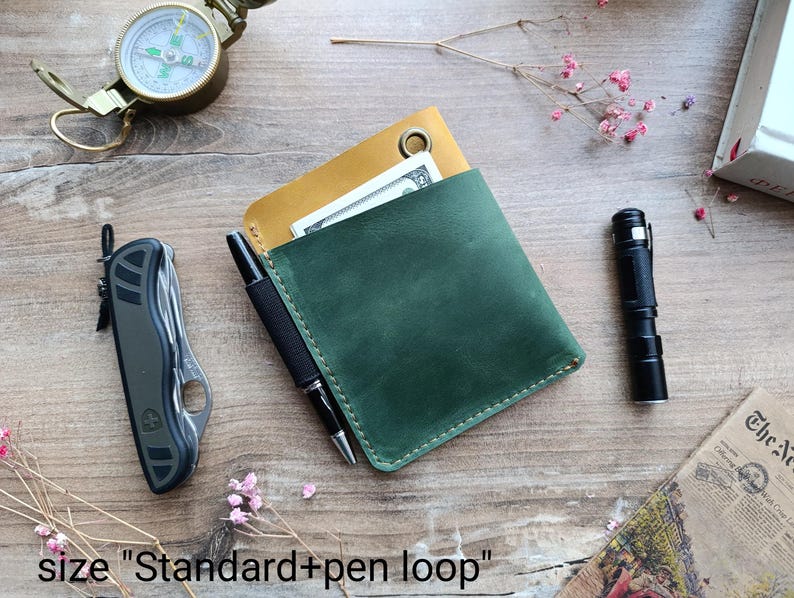 May include: A green leather wallet with a yellow leather flap and a pen loop. The wallet is closed and has a stitching detail around the edges. The text "size "Standard + pen loop"" is visible at the bottom of the image.