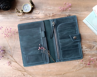 May include: A teal leather wallet with multiple card slots, a zippered pocket, and a snap closure. The wallet is open and lying on a wooden surface.