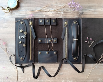 May include: A brown leather jewelry roll with multiple compartments for storing earrings, necklaces, and rings. The roll has a zipper closure and a tie closure.