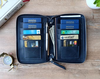 May include: A black leather passport holder with blue stitching, open to reveal multiple credit cards and passports. The passports are labeled "UKRAINE PASSPORT" in Ukrainian.