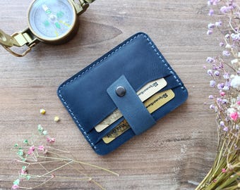 May include: A dark blue leather card holder with a flap closure and a snap button. The card holder has two slots for cards and is shown with two cards inserted.