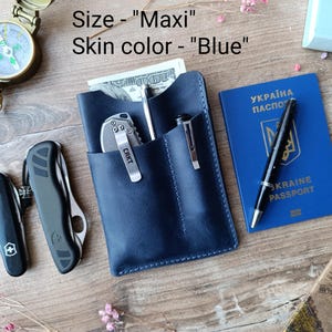 May include: A blue leather wallet with a pen and a pocket knife. The wallet has a stitched edge and the text "Size - "Maxi" Skin color - "Blue" ".