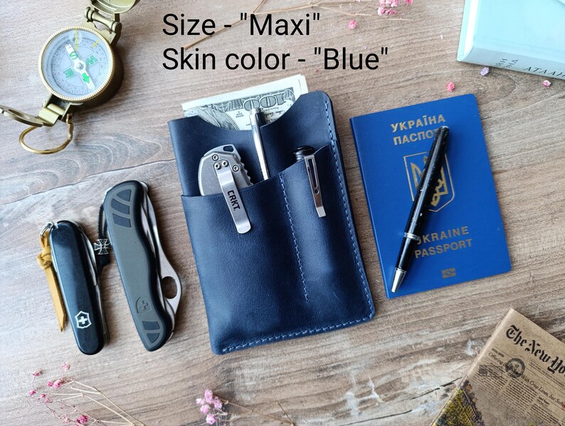 May include: A blue leather wallet with a pen and a pocket knife. The wallet has a stitched edge and the text "Size - "Maxi" Skin color - "Blue" ".