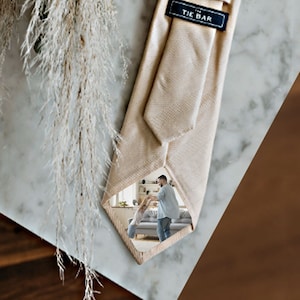 Pode incluir: Uma gravata bege com uma etiqueta de madeira que diz "The Tie Bar" e uma foto de um casal dançando no fundo.