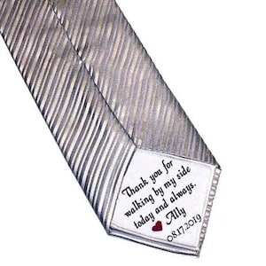 May include: A silver striped tie with a white tag attached. The tag has the text "Thank you for walking by my side today and always. Ally 08.17.2019" with a red heart.