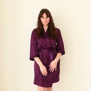May include: A purple satin robe with a tie belt. The robe has long sleeves and a V-neck.