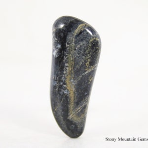 May include: A polished, elongated gemstone with a dark gray base color, accented by swirling patterns of gold and white. The stone has a smooth, glossy surface and a rounded shape, perfect for jewelry or collecting.