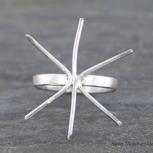 May include: Silver ring setting with six prongs, ready to be set with a gemstone. The ring band is textured.