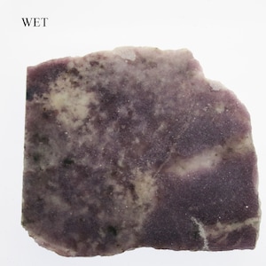 May include: A rectangular, rough-edged stone slab with a mottled pattern of deep purple, light purple, and off-white hues. The word "WET" is printed in black at the top. The stone has a slightly granular texture.