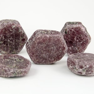 May include: Five rough, dark red ruby gemstones with a hexagonal shape. The gemstones have a natural, unpolished finish.