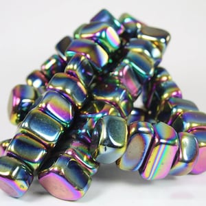 May include: A pile of iridescent, faceted, black hematite gemstone beads. The beads are in a variety of shapes and sizes, and they have a rainbow sheen.