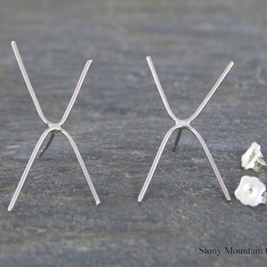 May include: Two silver earring settings with prongs in an X shape. The settings are designed to hold a gemstone or other embellishment. The settings are shown with two silver earring backs.