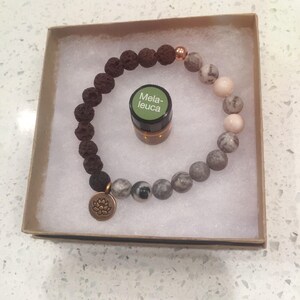 May include: A brown lava rock bracelet with a silver charm and a small bottle of essential oil labeled "Melaleuca".