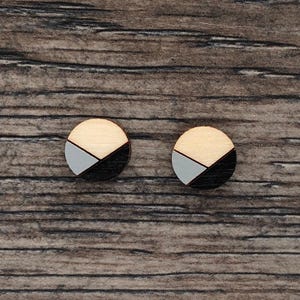May include: A pair of wooden stud earrings. Each earring is a circle divided into three sections: natural wood, light grey, and black. The earrings are displayed on a wooden surface.