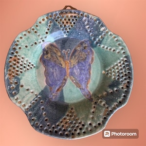 May include: A ceramic plate with a blue and green butterfly design. The plate has a scalloped edge and a pattern of holes around the rim.